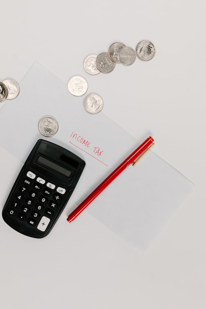 Calculator, pen, and coins on an envelope labeled Income Tax for tax preparation.