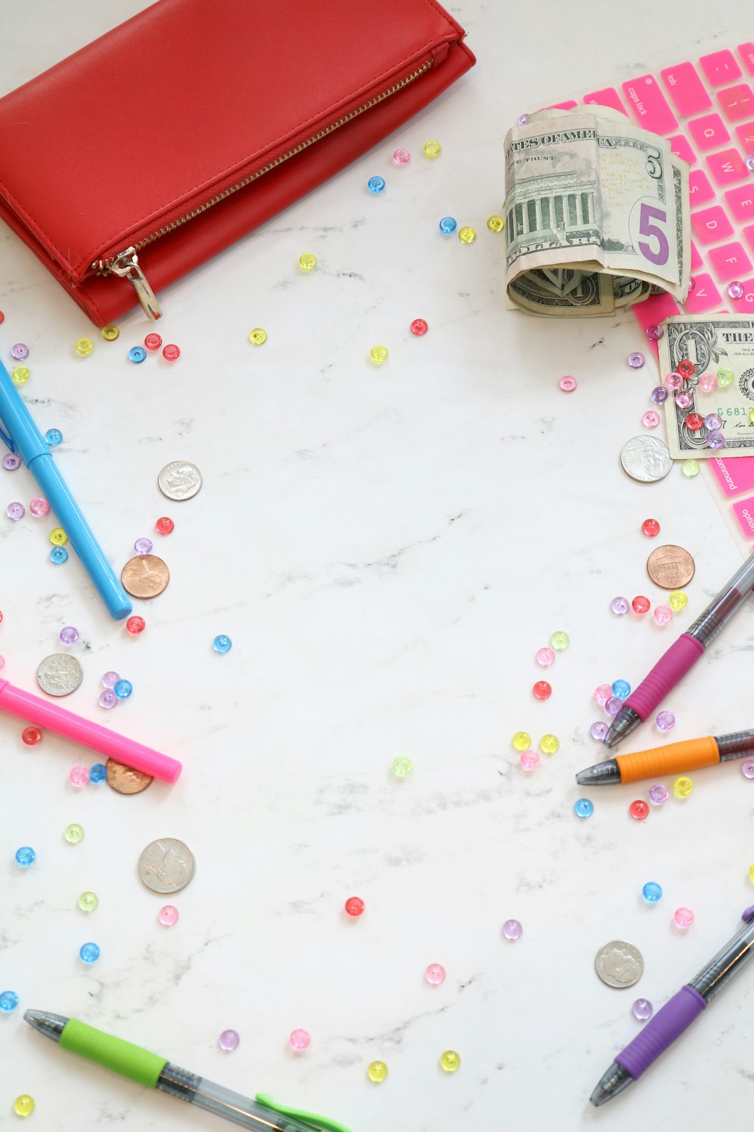 Marble money stock photo and money styled stock photo for personal finance bloggers, business coaches, and entrepreneurs with a pink keyboard, colorful pens, cash, a red wallet, and more.