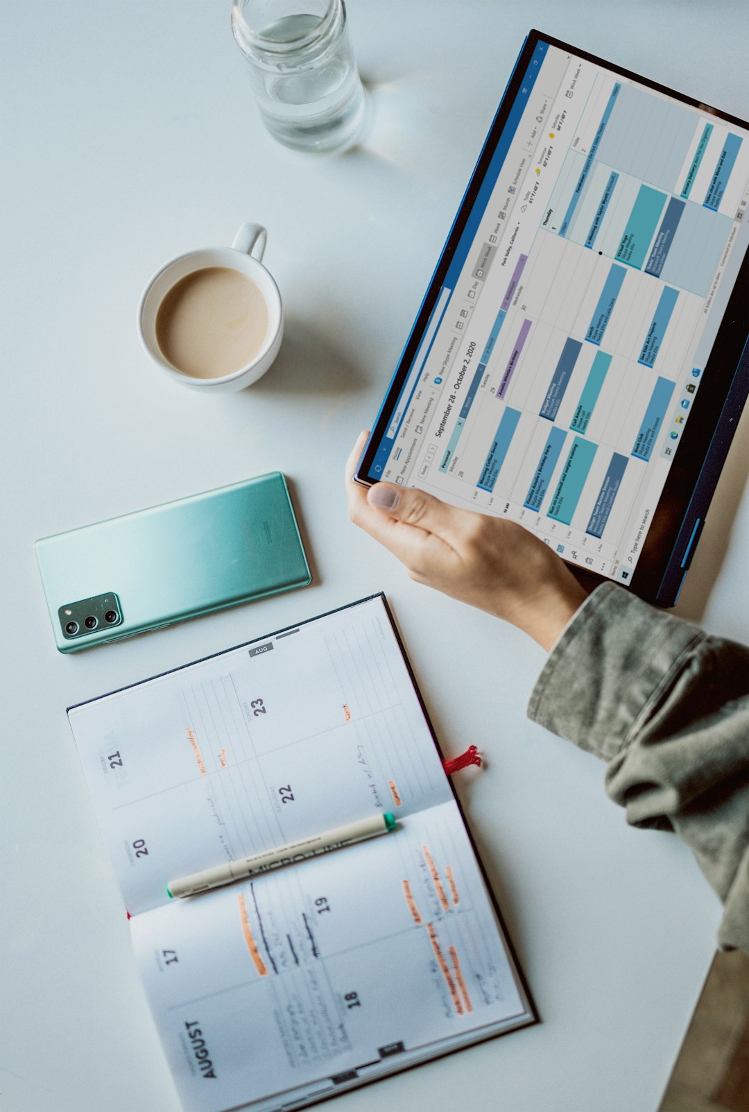 person holding a tablet near white ceramic mug and notebook